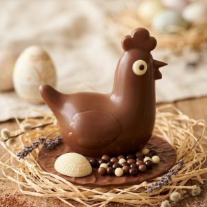 Moule poule en chocolat sur un socle en chocolat avec une crête, un demi oeuf praliné et des petites billes chocolat.